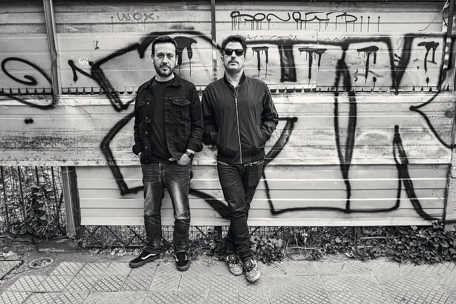 Dos integrantes de pie frente a un muro de grafitis
